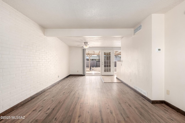 empty room with a textured ceiling, visible vents, baseboards, brick wall, and wood finished floors