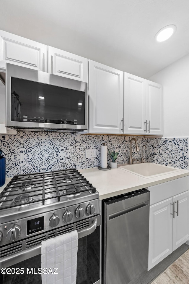 kitchen featuring appliances with stainless steel finishes, light countertops, a sink, and white cabinetry