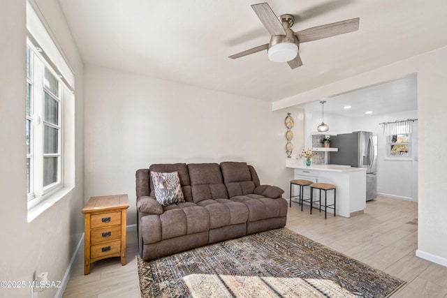 living room with light wood-type flooring, ceiling fan, and baseboards