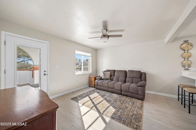 living area featuring light wood-style floors, baseboards, a ceiling fan, and beamed ceiling