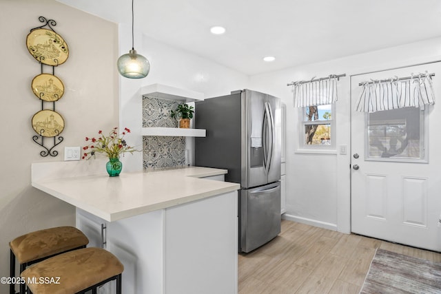 kitchen featuring a breakfast bar, light countertops, light wood-type flooring, open shelves, and stainless steel fridge