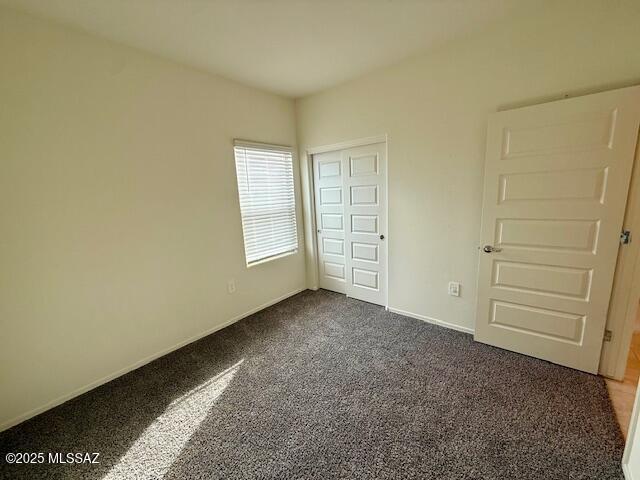 unfurnished bedroom with baseboards, dark carpet, and a closet