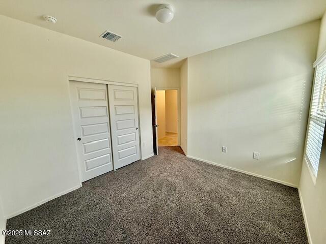 unfurnished bedroom with baseboards, visible vents, dark colored carpet, and a closet