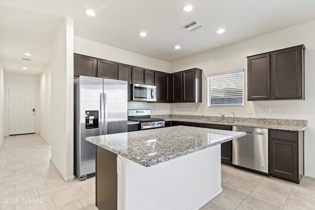 kitchen with visible vents, light stone counters, a center island, stainless steel appliances, and a sink