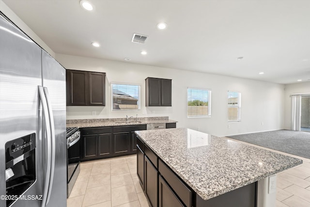 kitchen featuring light stone counters, stainless steel refrigerator with ice dispenser, a sink, and recessed lighting