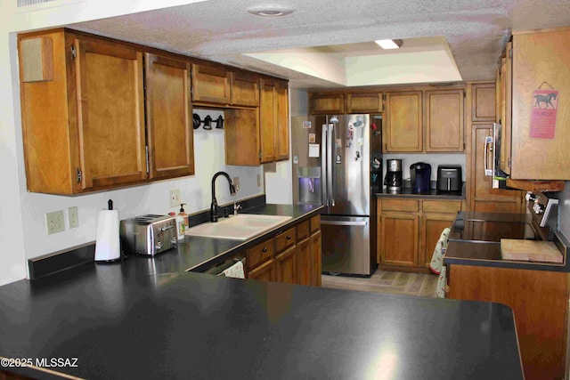 kitchen with brown cabinetry, a tray ceiling, a sink, and stainless steel fridge with ice dispenser