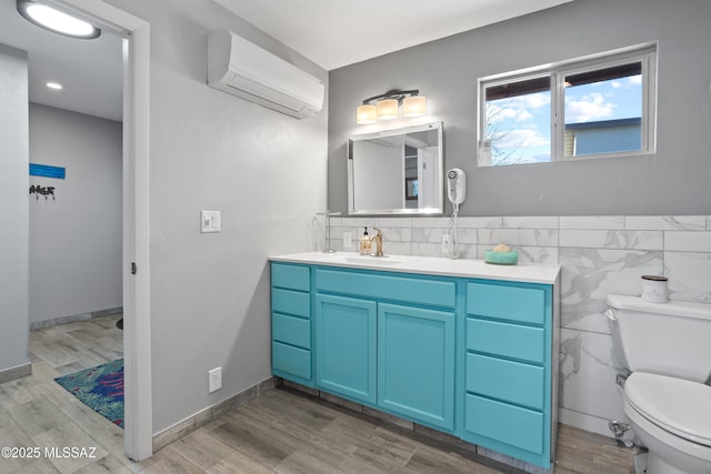 bathroom with a wall unit AC, toilet, wood finished floors, and vanity