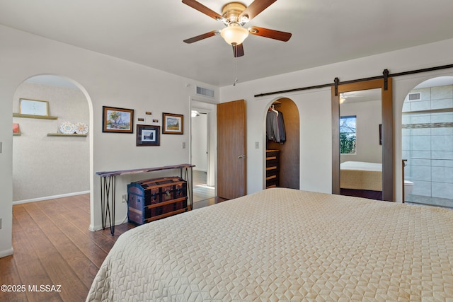 bedroom with arched walkways, a barn door, visible vents, wood-type flooring, and a walk in closet