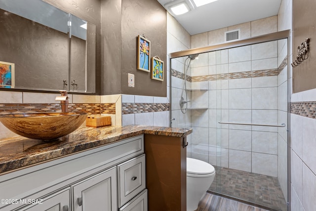 bathroom with tile walls, visible vents, toilet, a stall shower, and vanity