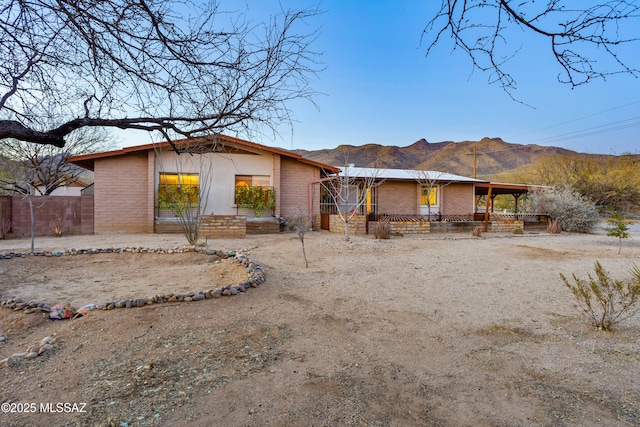 view of front facade with dirt driveway, fence, a mountain view, and brick siding