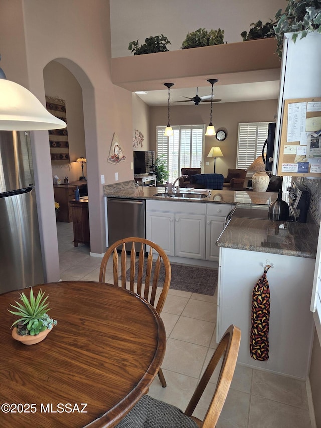 kitchen with light tile patterned floors, a peninsula, stainless steel appliances, white cabinetry, and a sink