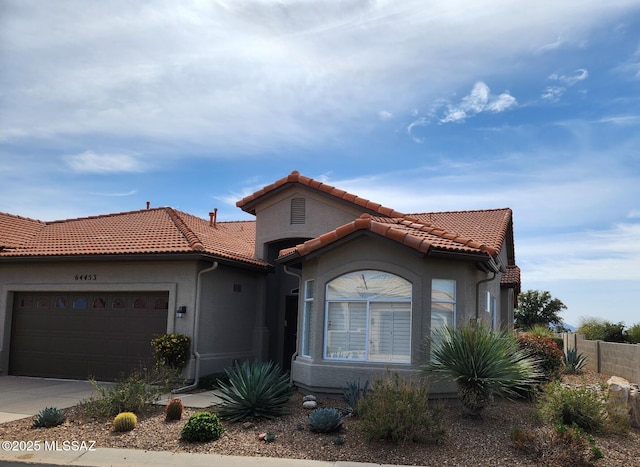 mediterranean / spanish-style house featuring an attached garage, stucco siding, driveway, and a tiled roof