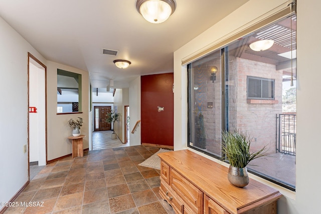 hall with stone finish floor, baseboards, and visible vents