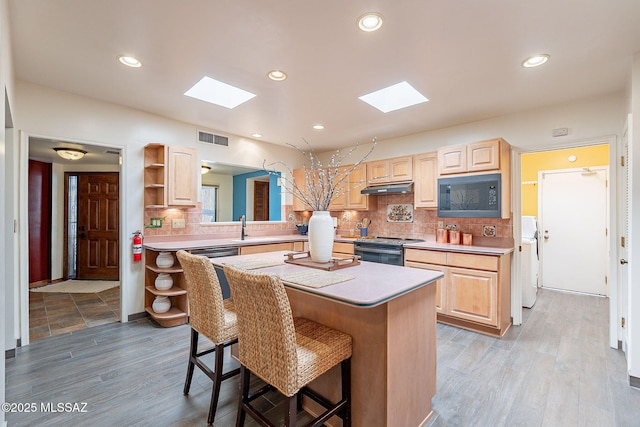 kitchen with range with electric stovetop, visible vents, light brown cabinetry, black microwave, and a kitchen breakfast bar