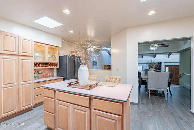 kitchen featuring recessed lighting, wood finished floors, a center island, decorative backsplash, and glass insert cabinets