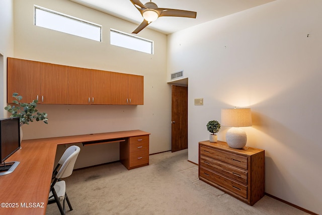 office area with light carpet, visible vents, a ceiling fan, built in study area, and a towering ceiling