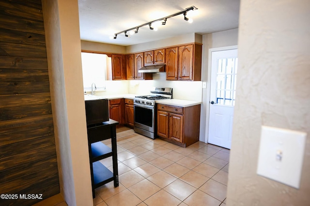 kitchen featuring light tile patterned floors, stainless steel gas range oven, a sink, exhaust hood, and light countertops