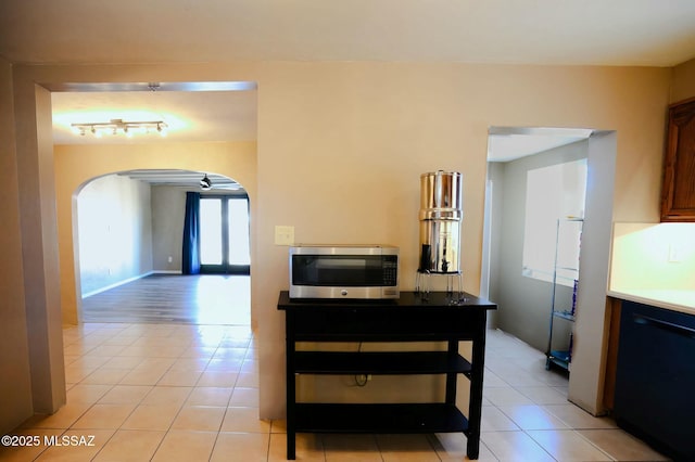 interior space with arched walkways, stainless steel microwave, light tile patterned flooring, dishwasher, and baseboards