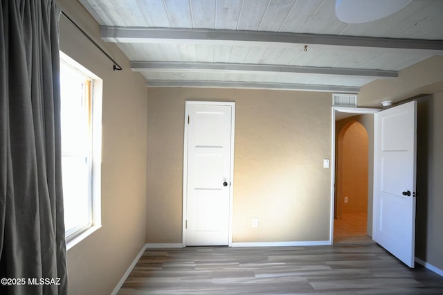 unfurnished bedroom with arched walkways, beam ceiling, visible vents, wood finished floors, and baseboards