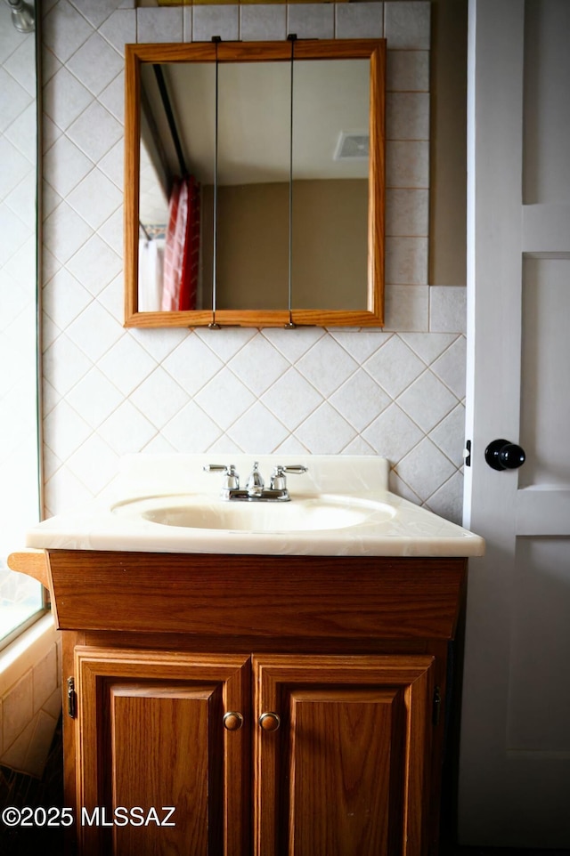 bathroom with tile walls, visible vents, vanity, and decorative backsplash