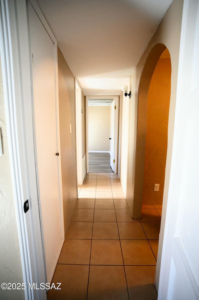 hallway with arched walkways and light tile patterned flooring