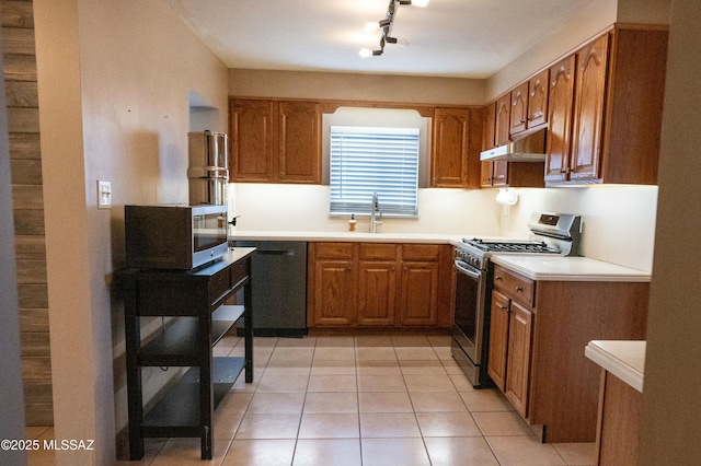 kitchen featuring light tile patterned floors, brown cabinetry, stainless steel appliances, under cabinet range hood, and a sink