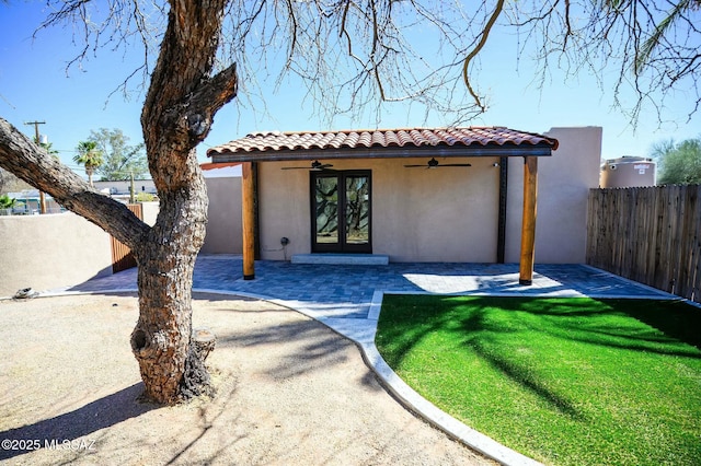 view of front of property featuring ceiling fan, a patio, a fenced backyard, a tiled roof, and stucco siding