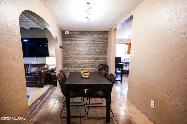 dining area with a textured ceiling, a textured wall, wood walls, and tile patterned flooring