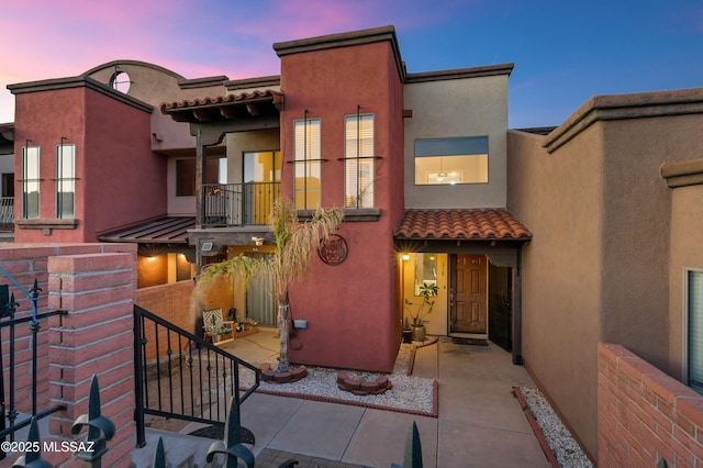 view of front of home with a tile roof, a patio, a balcony, and stucco siding