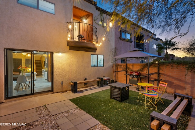 back of property at dusk featuring a patio, fence, a gazebo, and stucco siding