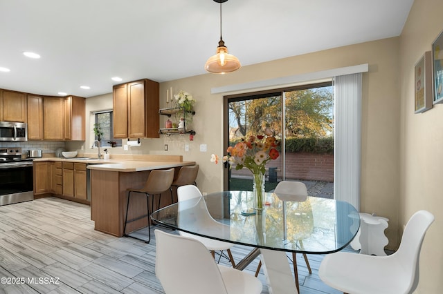 kitchen with a peninsula, a sink, light countertops, appliances with stainless steel finishes, and backsplash