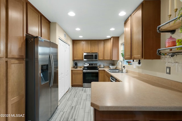 kitchen featuring brown cabinets, open shelves, decorative backsplash, appliances with stainless steel finishes, and a sink