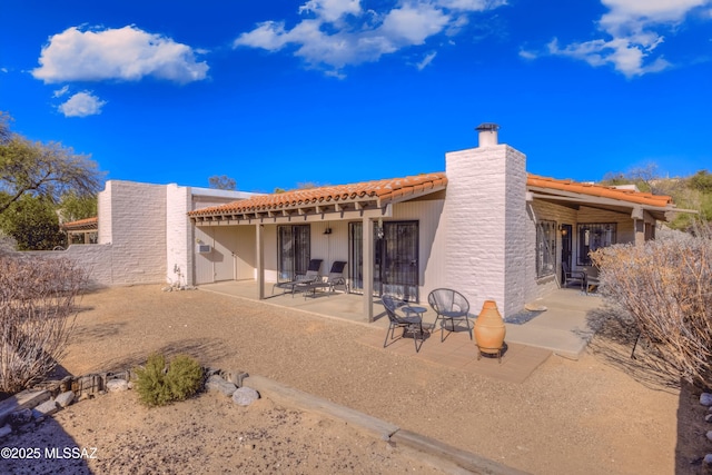 back of property with a tiled roof, a chimney, and a patio area