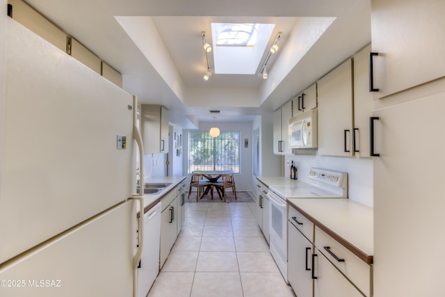 kitchen with white appliances, light tile patterned floors, a skylight, a tray ceiling, and light countertops