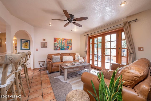 living area featuring arched walkways, a ceiling fan, a textured ceiling, french doors, and light tile patterned flooring