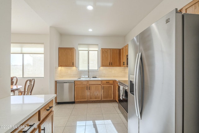 kitchen featuring light tile patterned floors, tasteful backsplash, light countertops, appliances with stainless steel finishes, and a sink