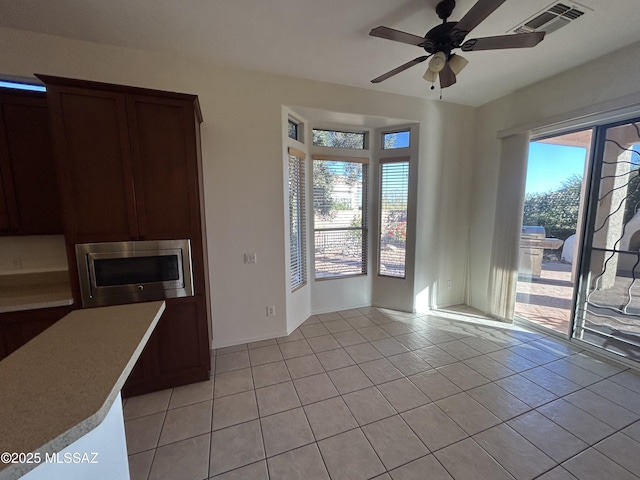 kitchen with light tile patterned floors, visible vents, a ceiling fan, stainless steel microwave, and light countertops