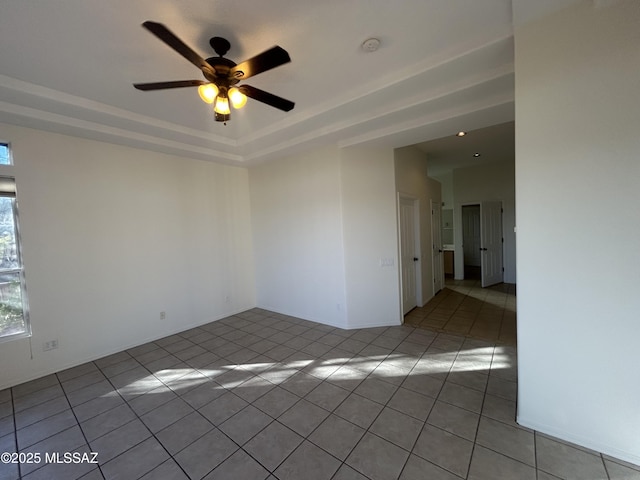 empty room with light tile patterned floors, ceiling fan, and a raised ceiling