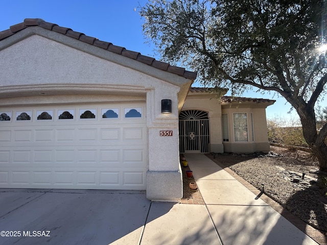 mediterranean / spanish-style home with a garage, concrete driveway, a tiled roof, and stucco siding