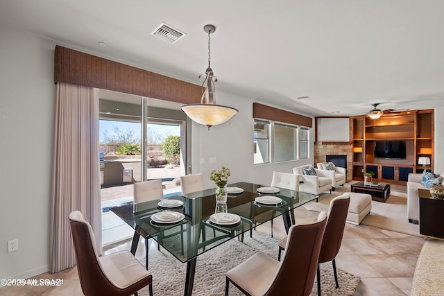 dining area featuring light tile patterned floors, ceiling fan, visible vents, and a glass covered fireplace