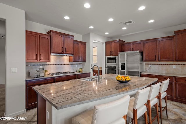 kitchen featuring stainless steel appliances, a sink, a kitchen breakfast bar, and light stone countertops