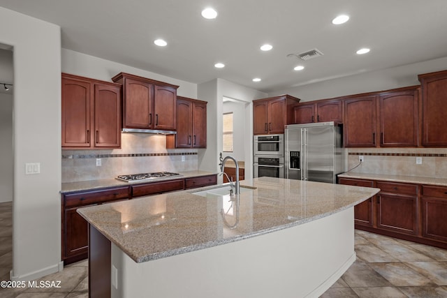 kitchen featuring a kitchen island with sink, appliances with stainless steel finishes, a sink, and light stone counters