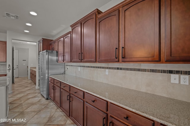 kitchen featuring light stone countertops, visible vents, decorative backsplash, and freestanding refrigerator