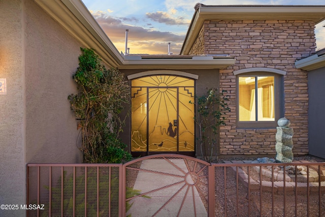 doorway to property featuring a gate, stone siding, fence, and stucco siding