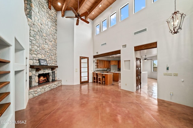 living room featuring visible vents, wooden ceiling, a stone fireplace, concrete floors, and ceiling fan with notable chandelier