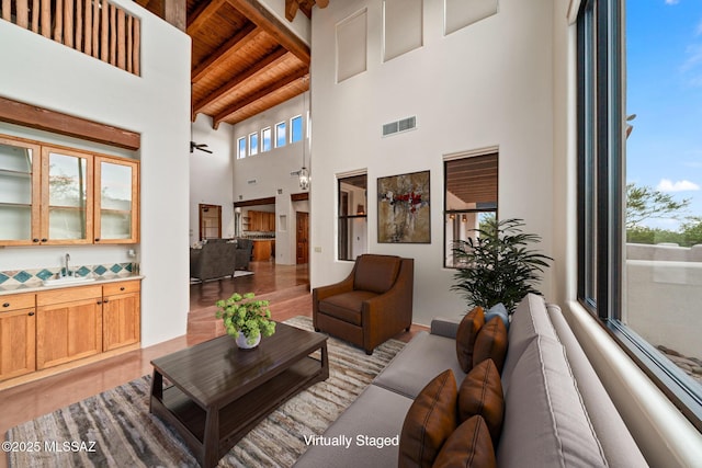 living area with wood ceiling, a high ceiling, visible vents, and beam ceiling