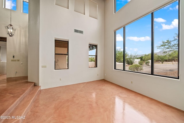 spare room with a high ceiling, an inviting chandelier, concrete floors, and visible vents