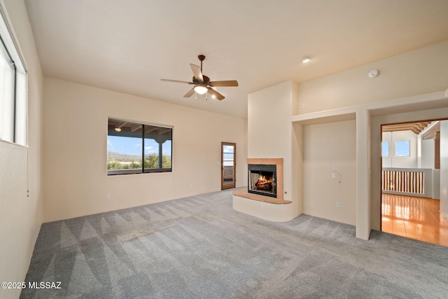 unfurnished living room featuring carpet floors, a lit fireplace, and a ceiling fan