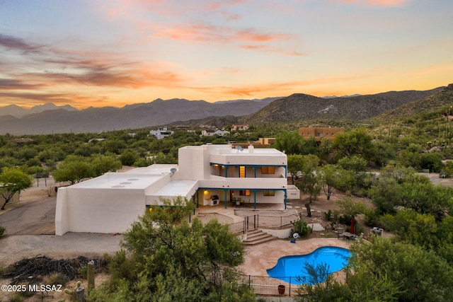 back of property at dusk featuring a patio, fence, a mountain view, and stucco siding