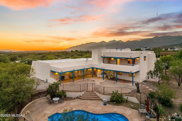 back of property at dusk with stairway, a patio area, a mountain view, and stucco siding